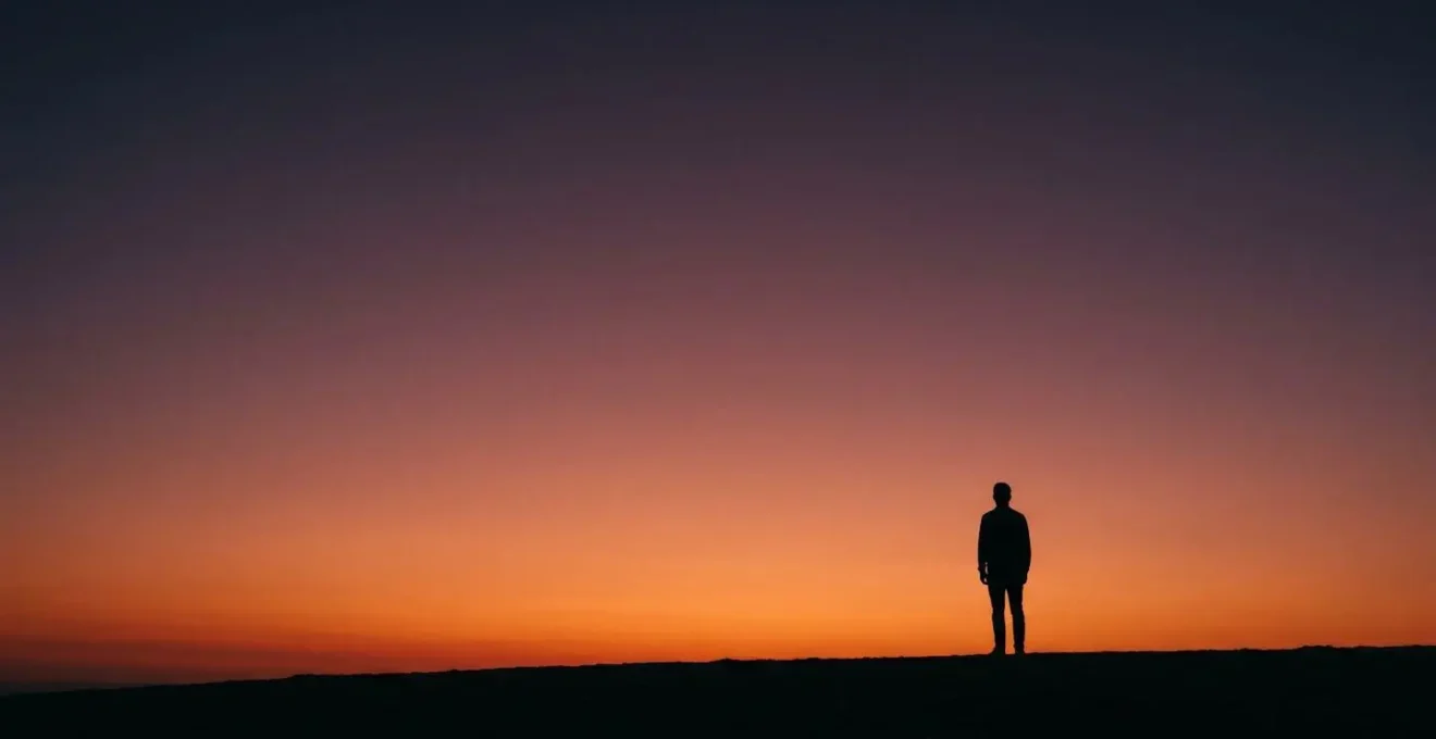 Wide environmental shot of a human silhouette against a vibrant sunset sky with intentional negative space